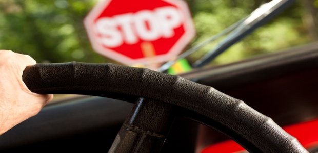 View over the windscreen with a hand holding a steering wheel and a blurred image of the STOP sign in front.