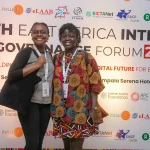 Nzambi J.Kakusu, Program Administrator, KICTANet, and Mitchelle Atieno standing behid the EAIGF 2024 banner during the East Africa Internet Governance Forum 2024.