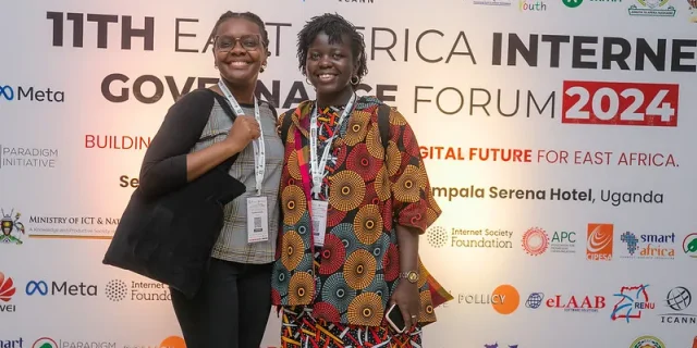 Nzambi J.Kakusu, Program Administrator, KICTANet, and Mitchelle Atieno standing behid the EAIGF 2024 banner during the East Africa Internet Governance Forum 2024.