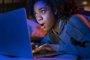 Close up of a woman typing on a keyboard. She seems surprised with her mouth agape.